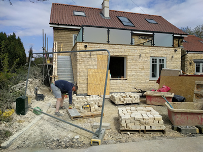 Ext. Day. Pub. Building the stone wall that encloses the staircase continues in fine weather.